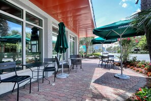 Enjoy a meal or coffee in the outdoor seating area with tables and chairs, shaded by umbrellas.