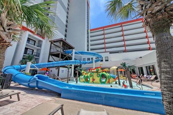 Enjoy the hotel's outdoor water park with a large water slide, play structure, and pool area featuring lounge chairs and umbrellas.