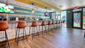 A bar area with a long counter, multiple stools, and a television screen. - Beautiful Resort! Cozy, 2 Room Junior Suite! (Myrtle Beach)