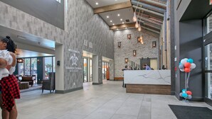 A modern hotel lobby with a reception desk, a seating area, and a view of the outside. - Beautiful Resort! Cozy, 2 Room Junior Suite! (Myrtle Beach)