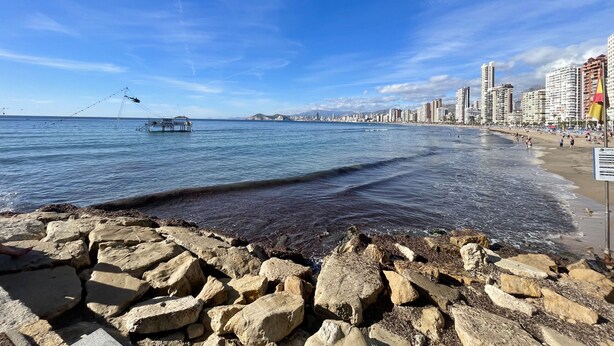 A coastal cityscape with a rocky shoreline, a fishing boat, and a beach with people. - ARIES CABLE SKI STUDIO R141 (Benidorm)