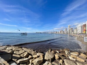 A coastal cityscape with a rocky shoreline, a fishing boat, and a beach with people. - ARIES CABLE SKI STUDIO R141 (Benidorm)