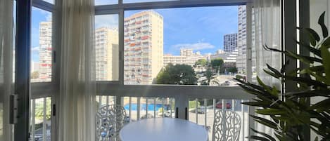 A balcony with a table and chairs, large windows with curtains, and a view of high-rise buildings.