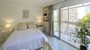 A bedroom with a bed, nightstands, a ceiling fan, a window with a view of buildings, and a potted plant. - ARIES CABLE SKI STUDIO R141 (Benidorm)