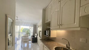 A modern kitchen with white cabinets, a stainless steel sink, and a dining area with a table and chairs. - ARIES CABLE SKI STUDIO R141 (Benidorm)
