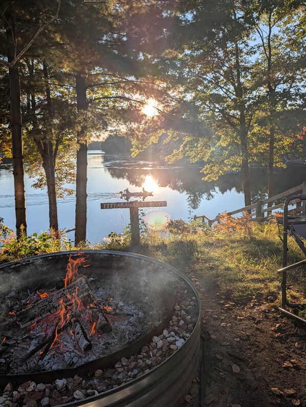 A campfire surrounded by trees with a lake in the background.
