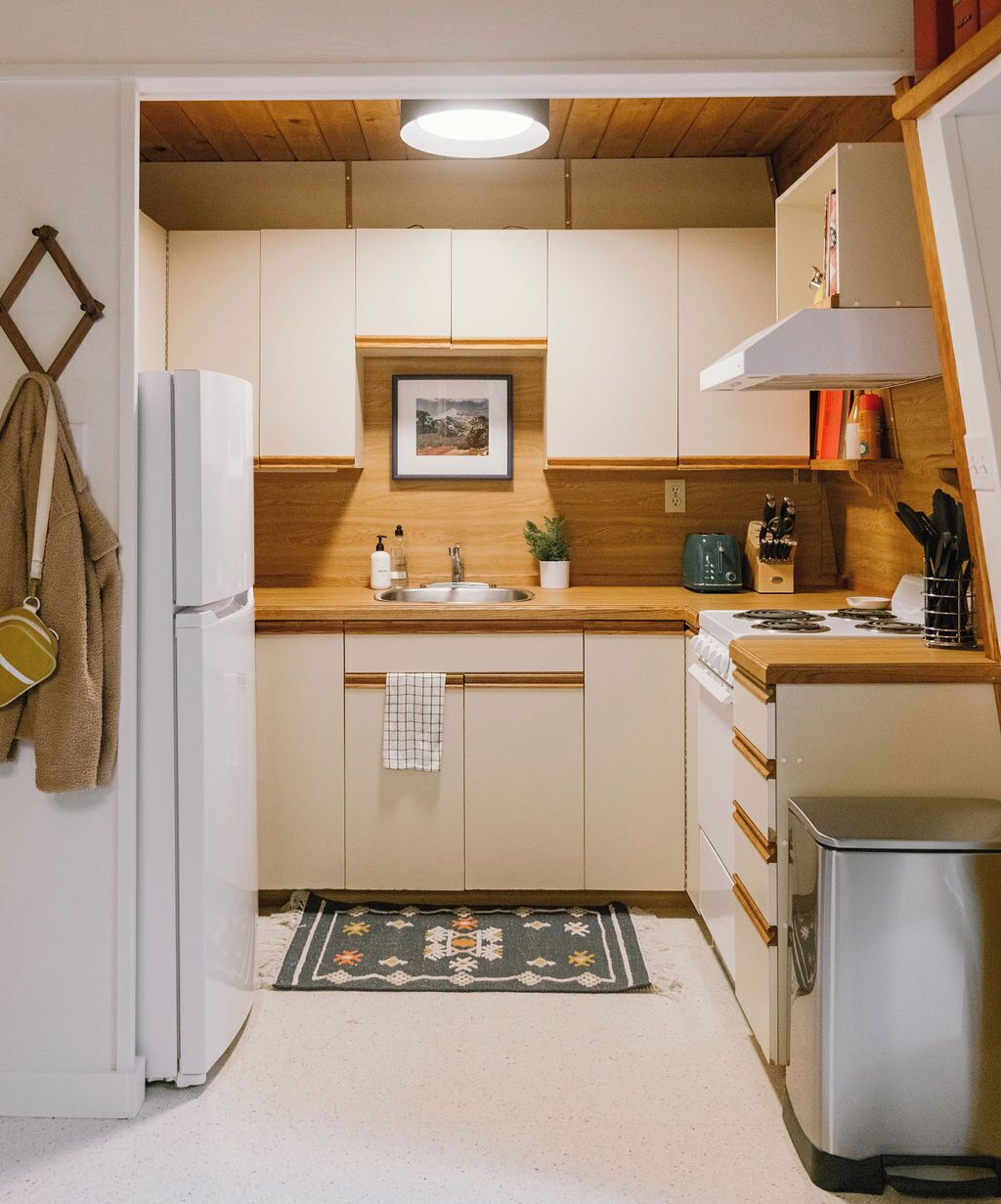 Una cocina compacta con armarios blancos, encimera de madera, un lavabo, estufa y un refrigerador pequeño.