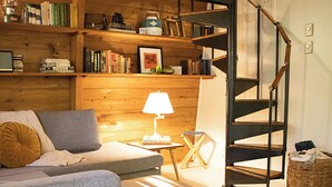 A cozy room with a sofa, a small table, a lamp, a bookshelf, and a spiral staircase. - Iconic Arched Cabin | Near Mt Baker Hiking (Deming)