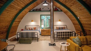 A cozy attic bedroom with two beds, a wooden ceiling, a small table, and a yellow sofa. - Iconic Arched Cabin | Near Mt Baker Hiking (Deming)