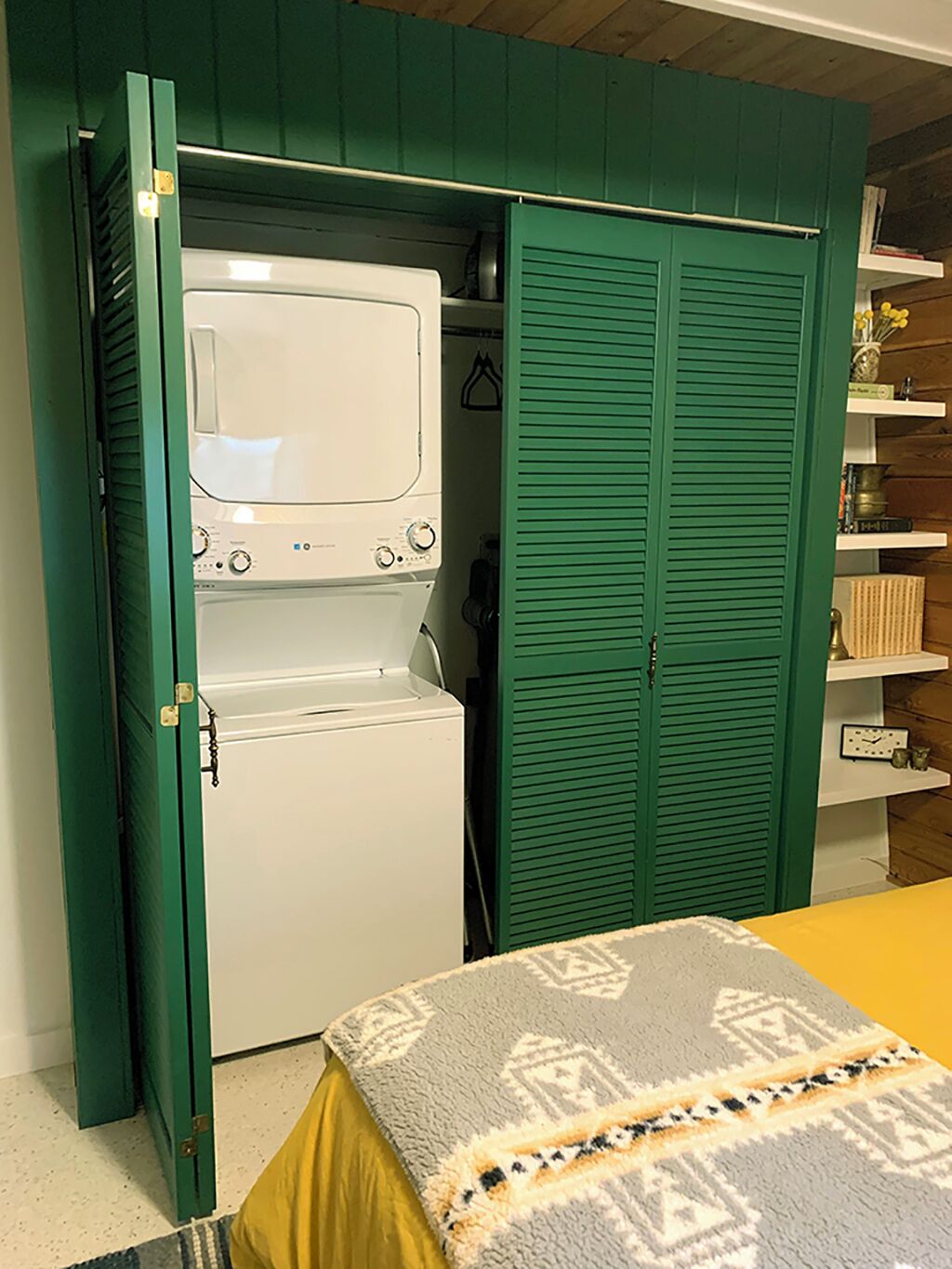 Een kleine kamer met een wasmachine en een groene garderobe.