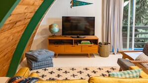 A cozy living room with a wooden ceiling, a television, a globe, and a sofa. - Iconic Arched Cabin | Near Mt Baker Hiking (Deming)