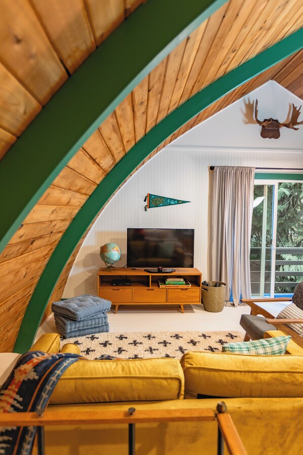 Una habitación en el ático con techo de madera, un televisor, un globo terráqueo y un sofá.