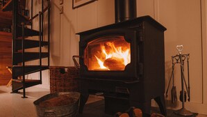 A wood-burning stove with a fire, a metal bucket, and a pair of boots on a mat. - Iconic Arched Cabin | Near Mt Baker Hiking (Deming)