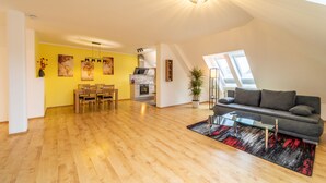 A spacious living area with a dining table and chairs, a sofa, and a kitchen in the background.
