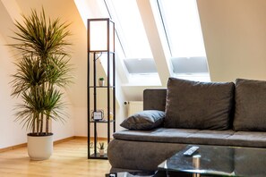 Una sala de estar moderna con un sofá gris, una planta alta en maceta, un estante negro y un tragaluz.