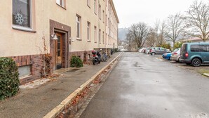 A narrow street with parked cars and a building with a brick facade and multiple windows.