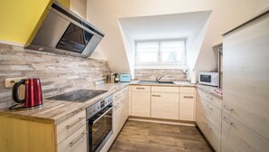 A compact kitchen with a built-in oven, a microwave, and a kettle on the countertop.