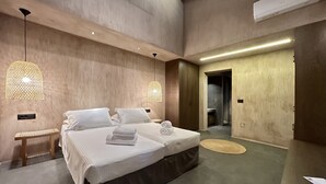 Una habitación de hotel moderna con una cama grande, dos mesitas de noche y un baño visible a través de una puerta abierta.
