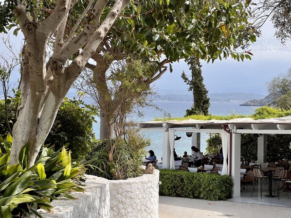 An outdoor dining area with stone walls and tables, overlooking a body of water and hills.