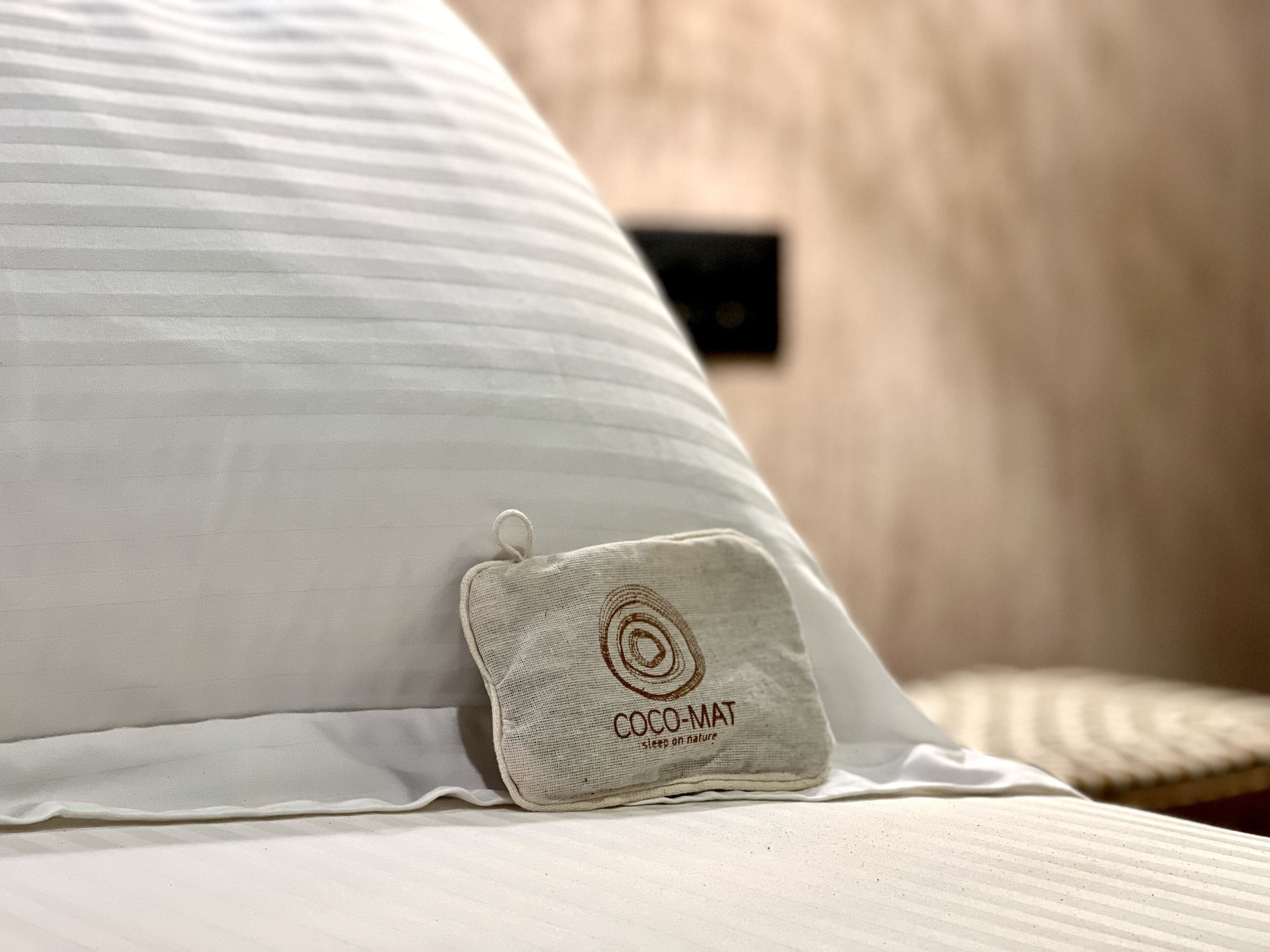 A bed with a white pillow and a small pillow with the text "COCO-MAT sleeps on nature".