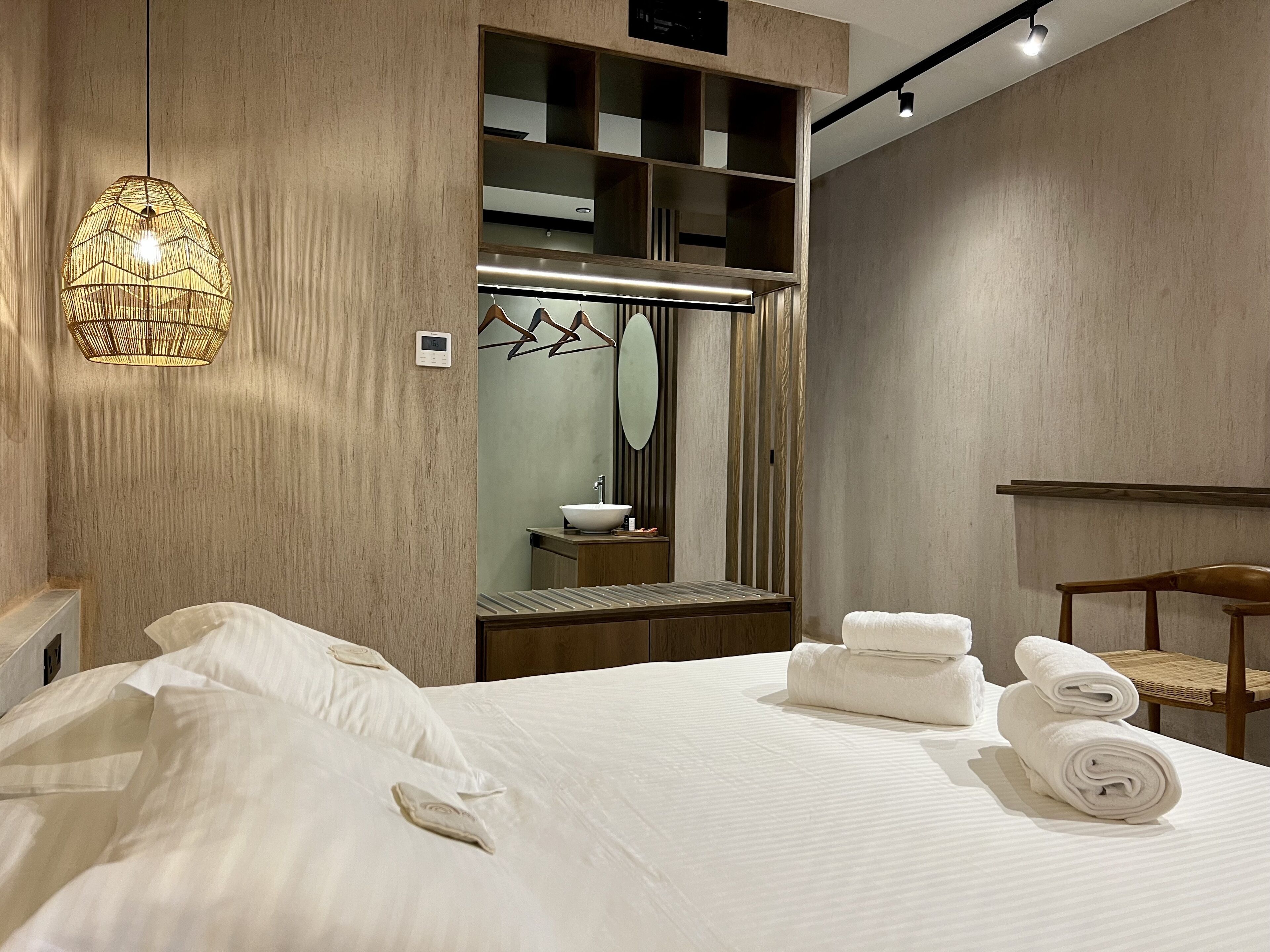Habitación de hotel con una cama grande, un armario de madera, un espejo y una lámpara colgante.