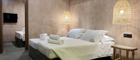 Une chambre d’hôtel moderne avec un grand lit, deux tables de chevet, une télévision et deux lampes suspendues.