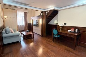 Ein Zimmer mit einer Couch, einem Schreibtisch, einem Stuhl, einer Treppe und einem Fenster.