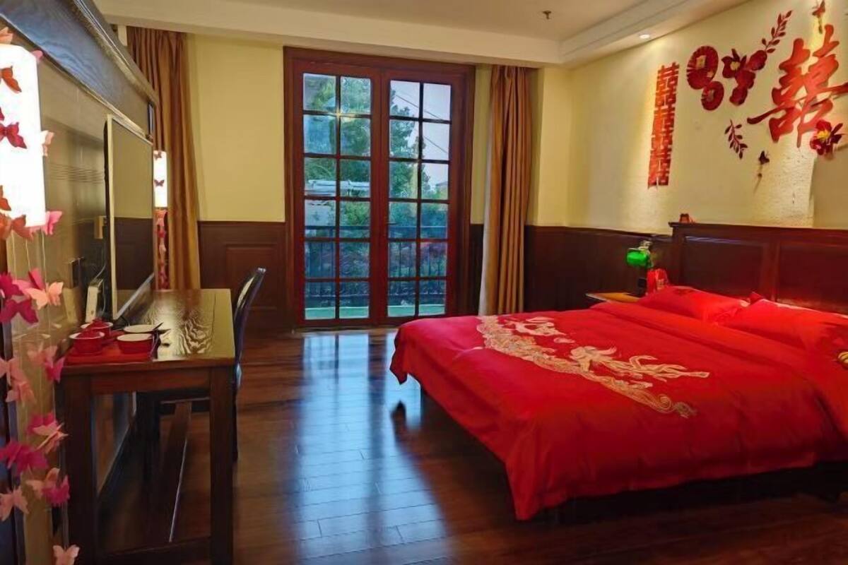 A hotel room with a large bed, a desk, and a view through a glass door.