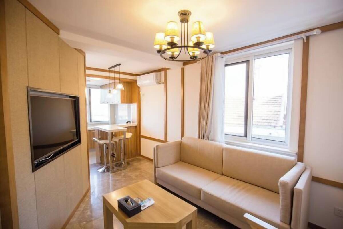 A compact living space with a sofa, a television, a small table, and a kitchenette in the background.