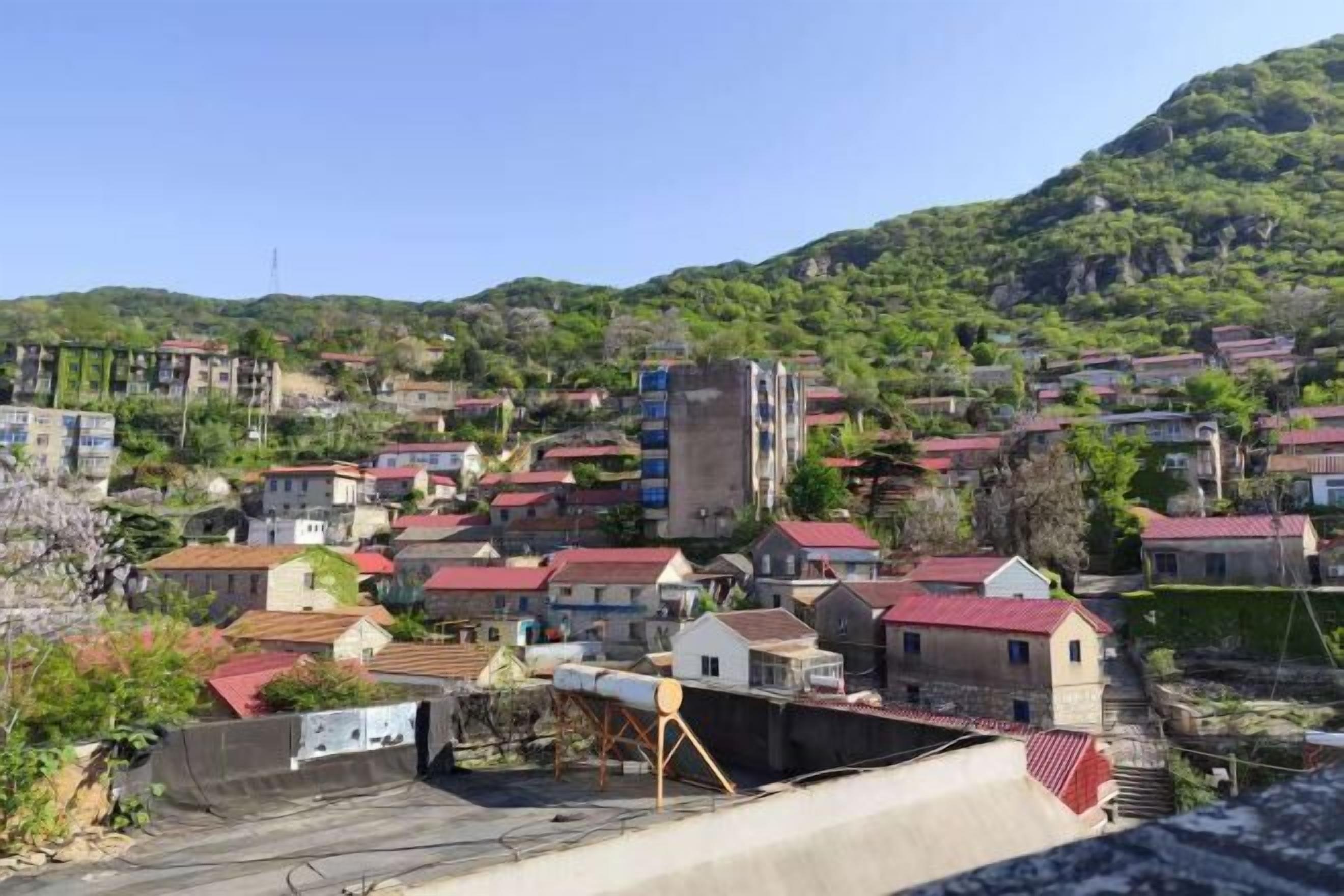 A residential area with houses, some with red roofs, and a hill in the background.