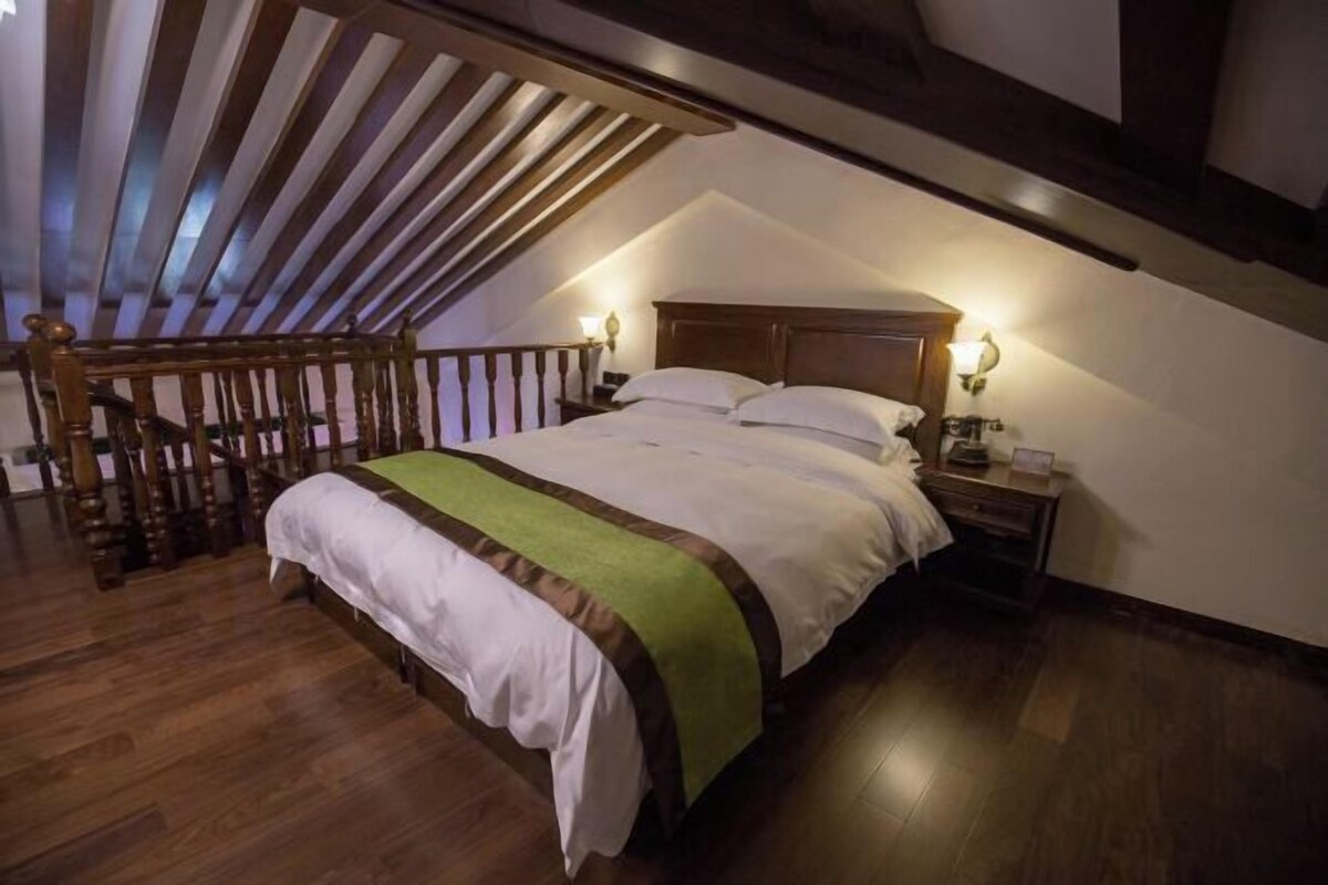 A bedroom with a sloped ceiling, wooden beams, a bed with white bedding, two bedside lamps, and a nightstand.