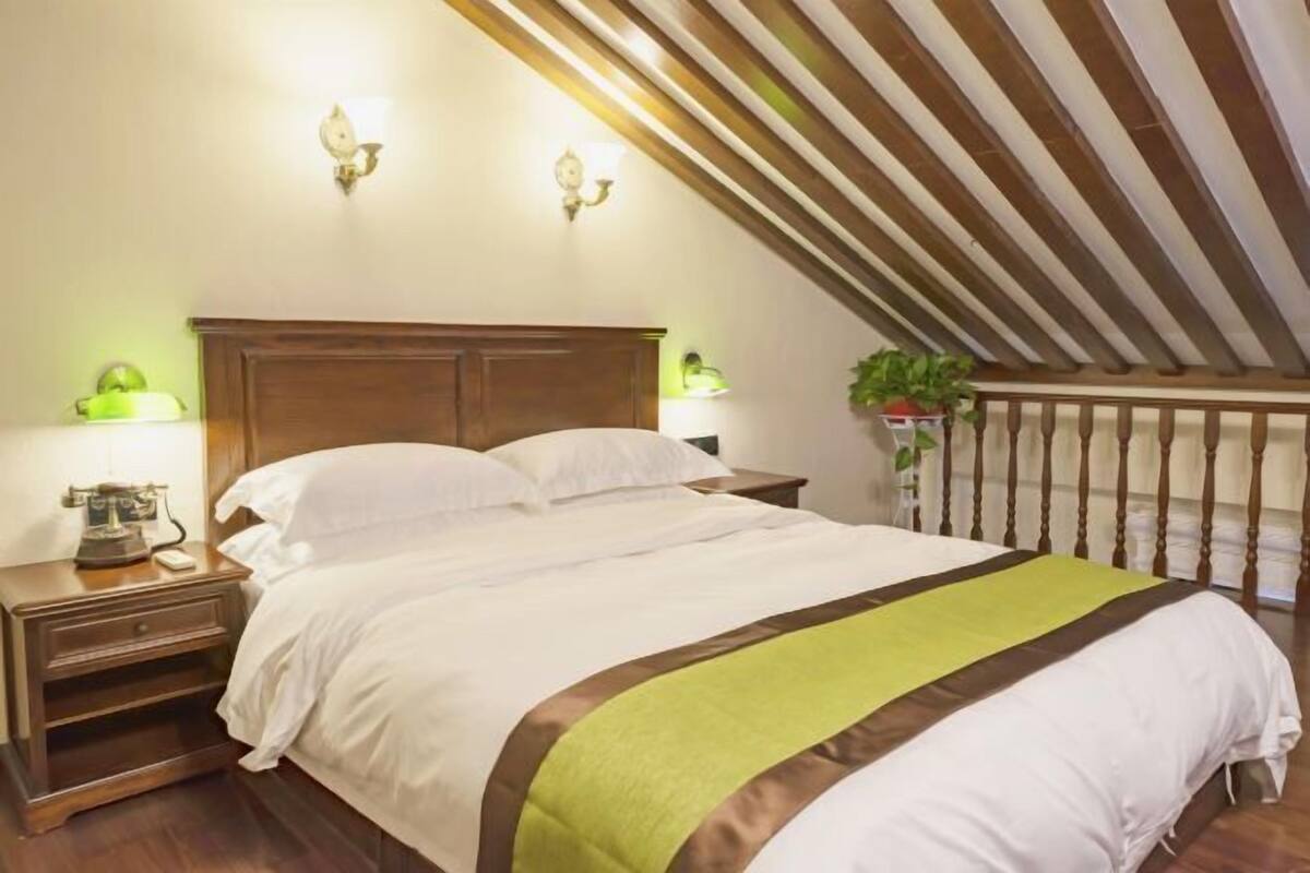 A bedroom with a wooden headboard, a bed with white bedding and a green accent, bedside tables with lamps, and a plant.