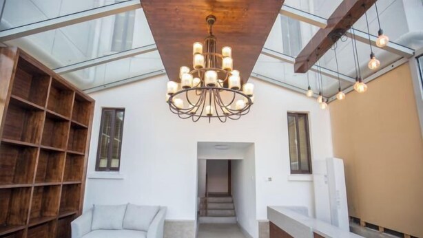 Un interior moderno con techo de vidrio, una lámpara central, un sofá, una estantería de madera y un mostrador de recepción.
