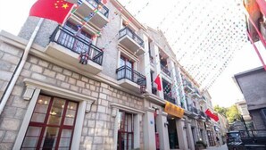 Un hotel de varios pisos con balcones, fachada de piedra y banderas rojas.
