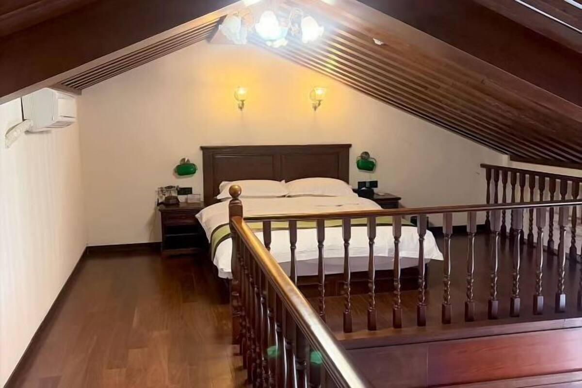 A bedroom with a wooden ceiling, a bed with white bedding, two wall-mounted lamps, and a wooden railing.