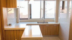 Una cocina moderna con armarios de madera, encimera blanca, pileta integrada y ventana que proporciona luz natural.