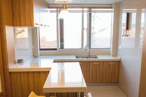A modern kitchen with wooden cabinets, a white countertop, a built-in sink, and a window providing natural light.