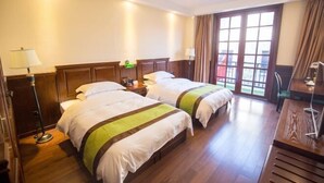 Habitación de hotel con dos camas, suelo de madera, ventilador de techo y un ventanal grande con cortinas.