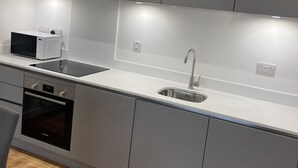 Une cuisine moderne avec des meubles gris, un évier en acier inoxydable, un four Bosch et un four à micro-ondes.