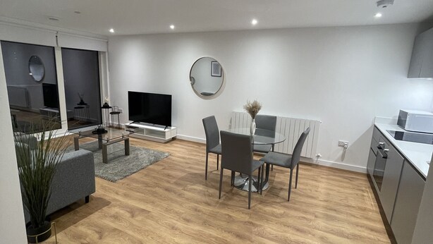 Un salon moderne avec un coin repas, un plancher en bois et une cuisine à l’arrière-plan.