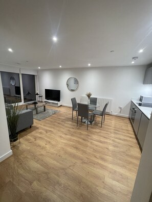 Uma sala de estar moderna com área de jantar, piso de madeira e cozinha ao fundo.