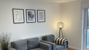 Un salon moderne avec un canapé gris, une table basse en verre et trois œuvres d’art encadrées accrochées au mur.