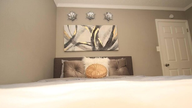 A bedroom with a bed, a headboard, a wall-mounted abstract painting, and a door. - Home Sweet Home Bungalow (North Little Rock)