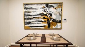 Une table à manger avec quatre verres et sous-tasses en verre transparent, placée devant un mur orné d’un grand tableau abstrait.