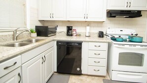 Une cuisine avec des meubles blancs, un lave-vaisselle, une cuisinière et un four à micro-ondes.