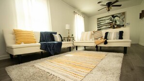 Un salon avec deux canapés blancs, un grand tapis à rayures et un ventilateur de plafond.