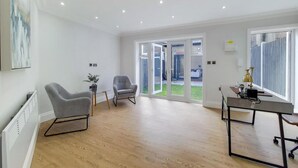 Une pièce moderne et bien éclairée, dotée d’un plancher en bois, d’un fauteuil gris, d’une petite table avec une plante et d’un bureau avec une lampe.
