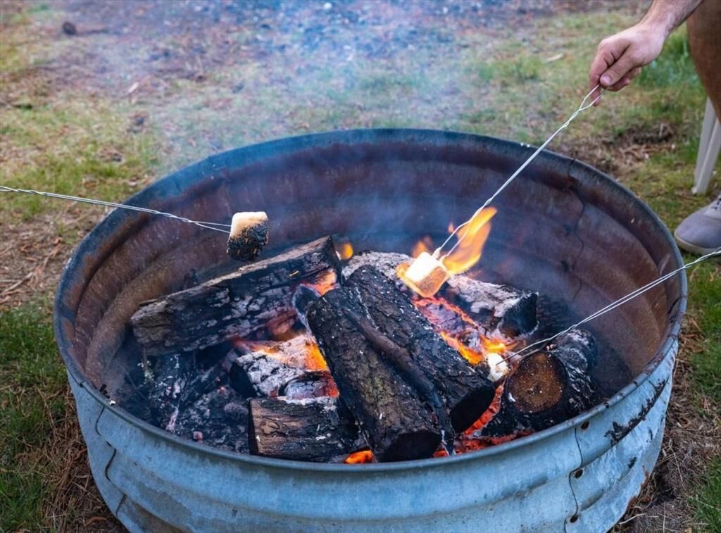 A metal fire pit with burning logs and a person holding a stick over the fire.
