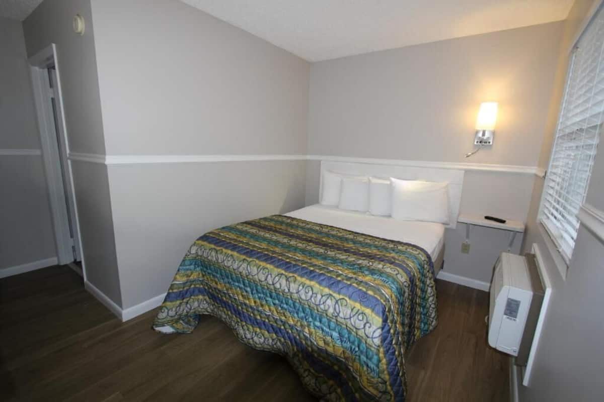 Habitación de hotel con cama, mesita de noche, lámpara de pared y radiador.