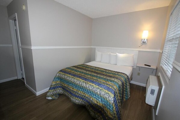 Habitación de hotel con cama, mesita de noche, lámpara de pared y radiador.